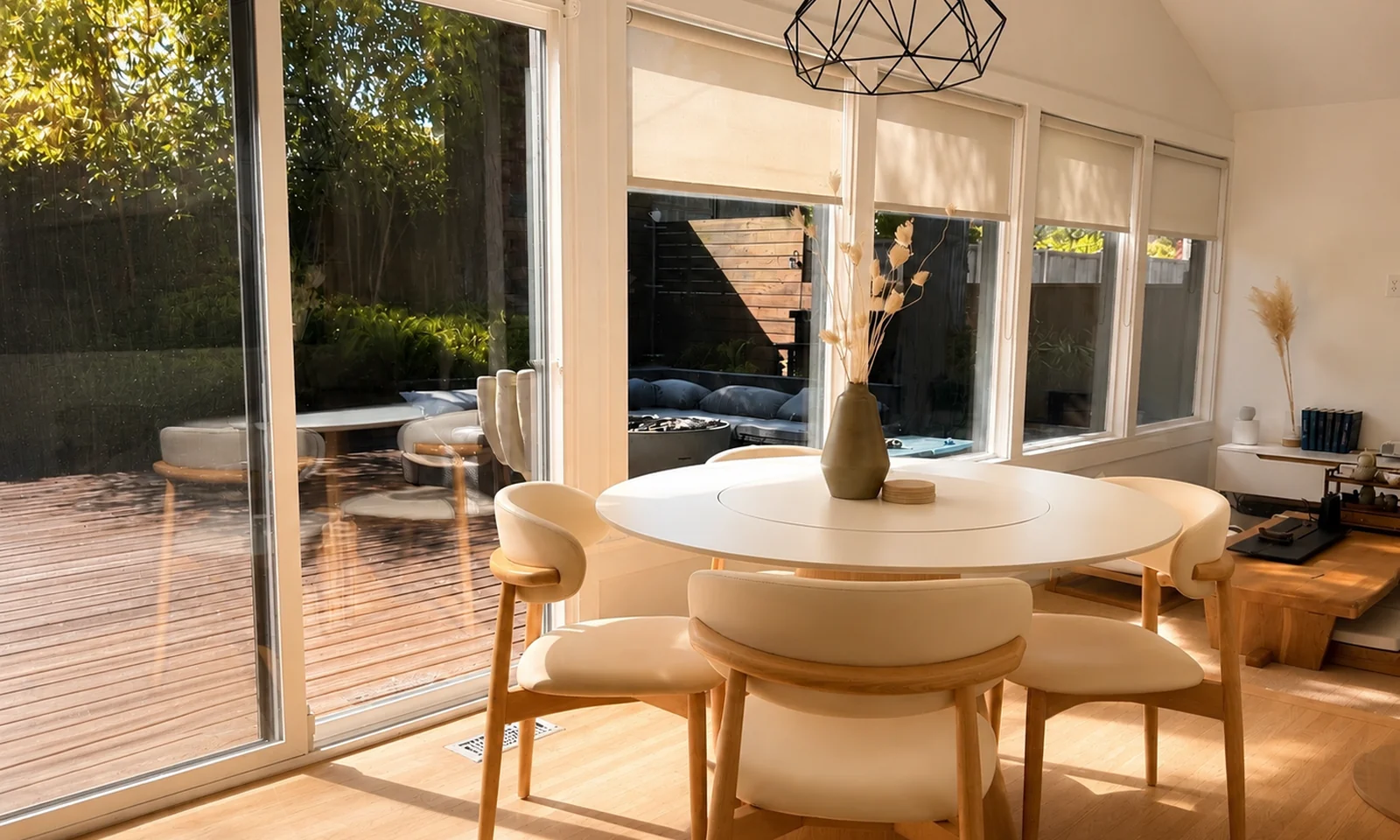 Round dining table with four chairs beside floor-to-ceiling windows, with the deck visible outside