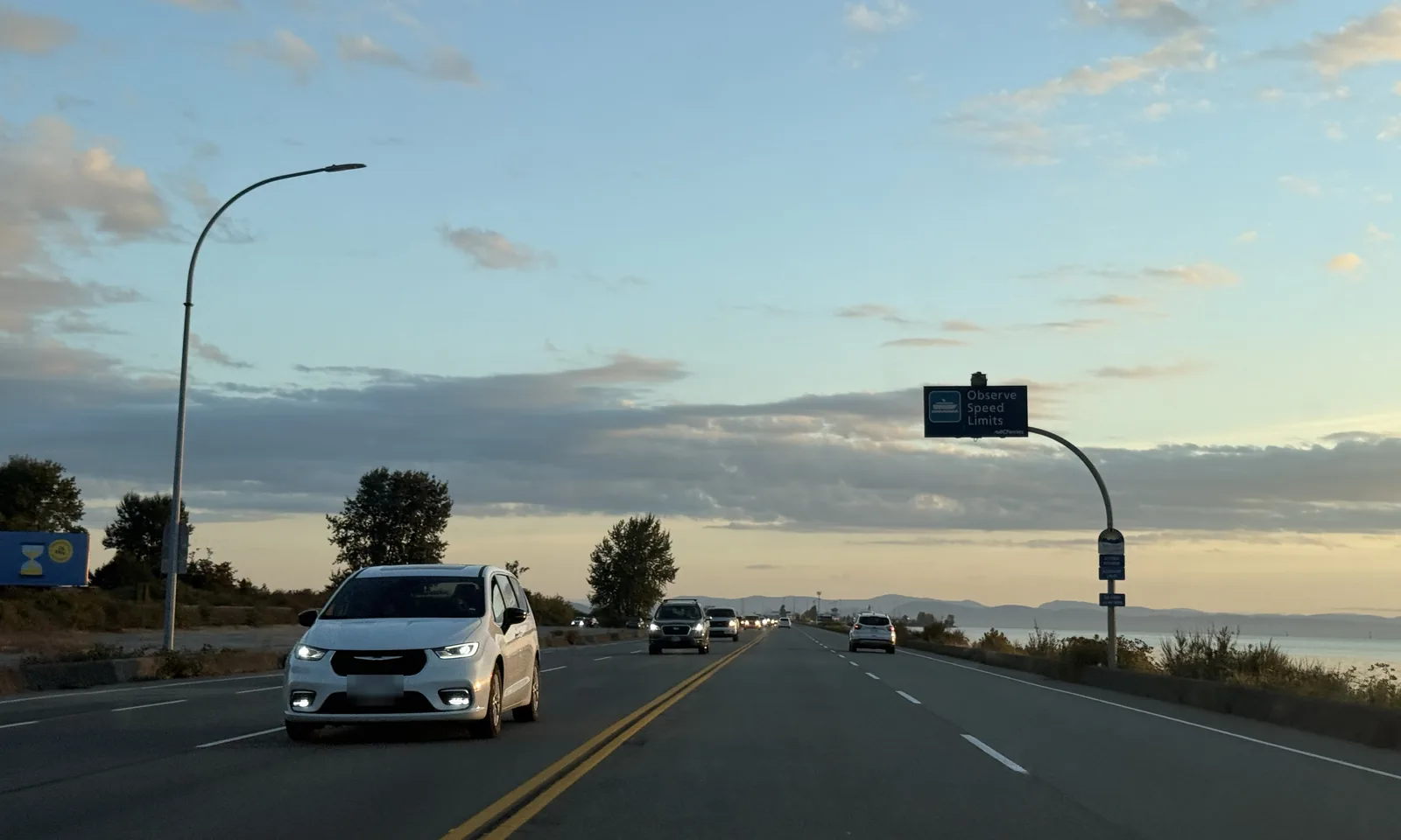 Highway 17 on the Tsawwassen causeway at dusk, a BC Ferries speed-limit sign overhead and the strait on the right