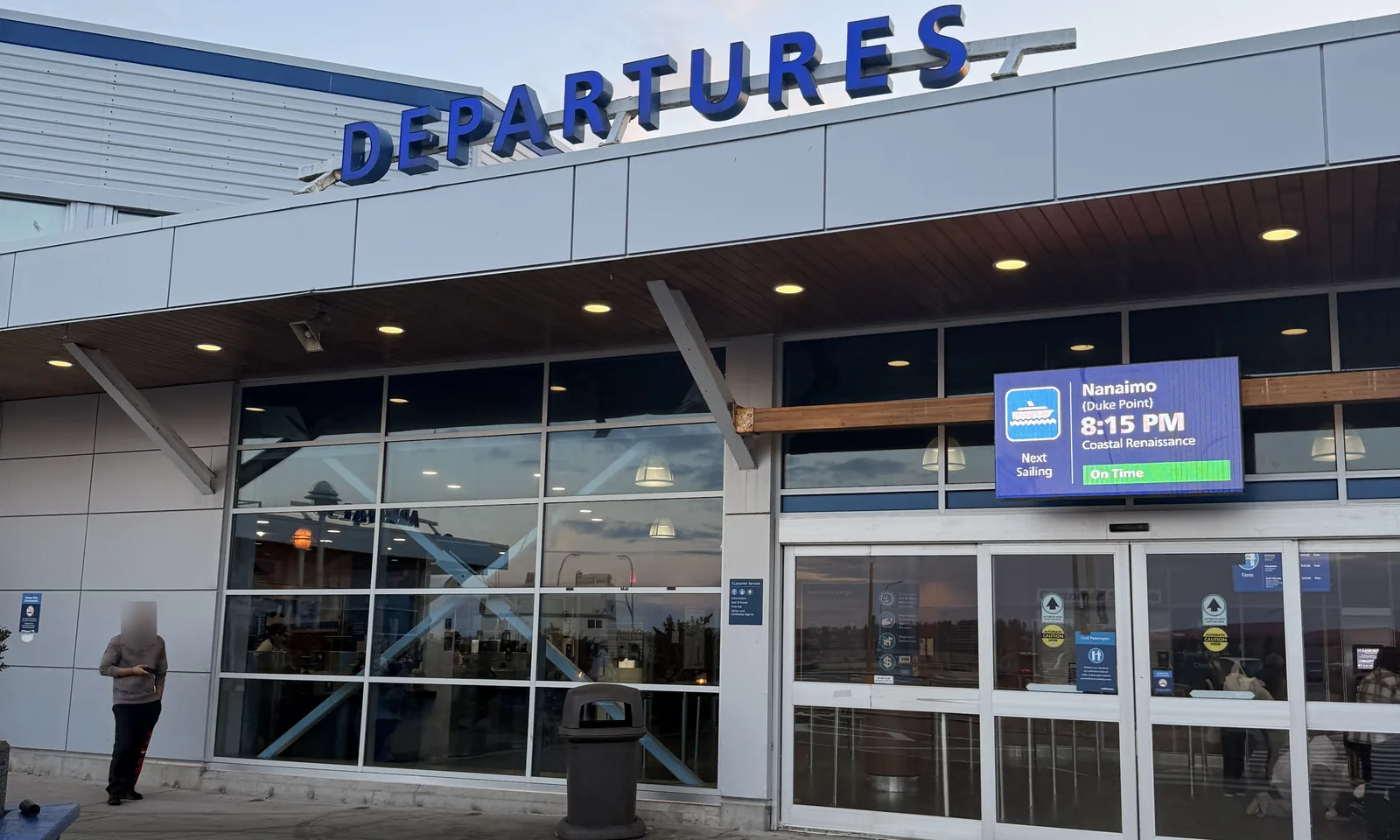 Departures entrance of the Tsawwassen Ferry Terminal building, with a screen showing the next sailing to Nanaimo (Duke Point) on time